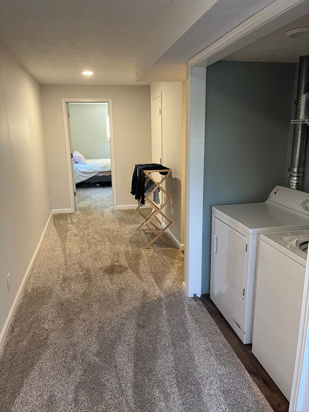 Refinished basement hallway with new plush carpet, fresh paint, white trim, recessed lighting, and an open laundry area with wood-look flooring