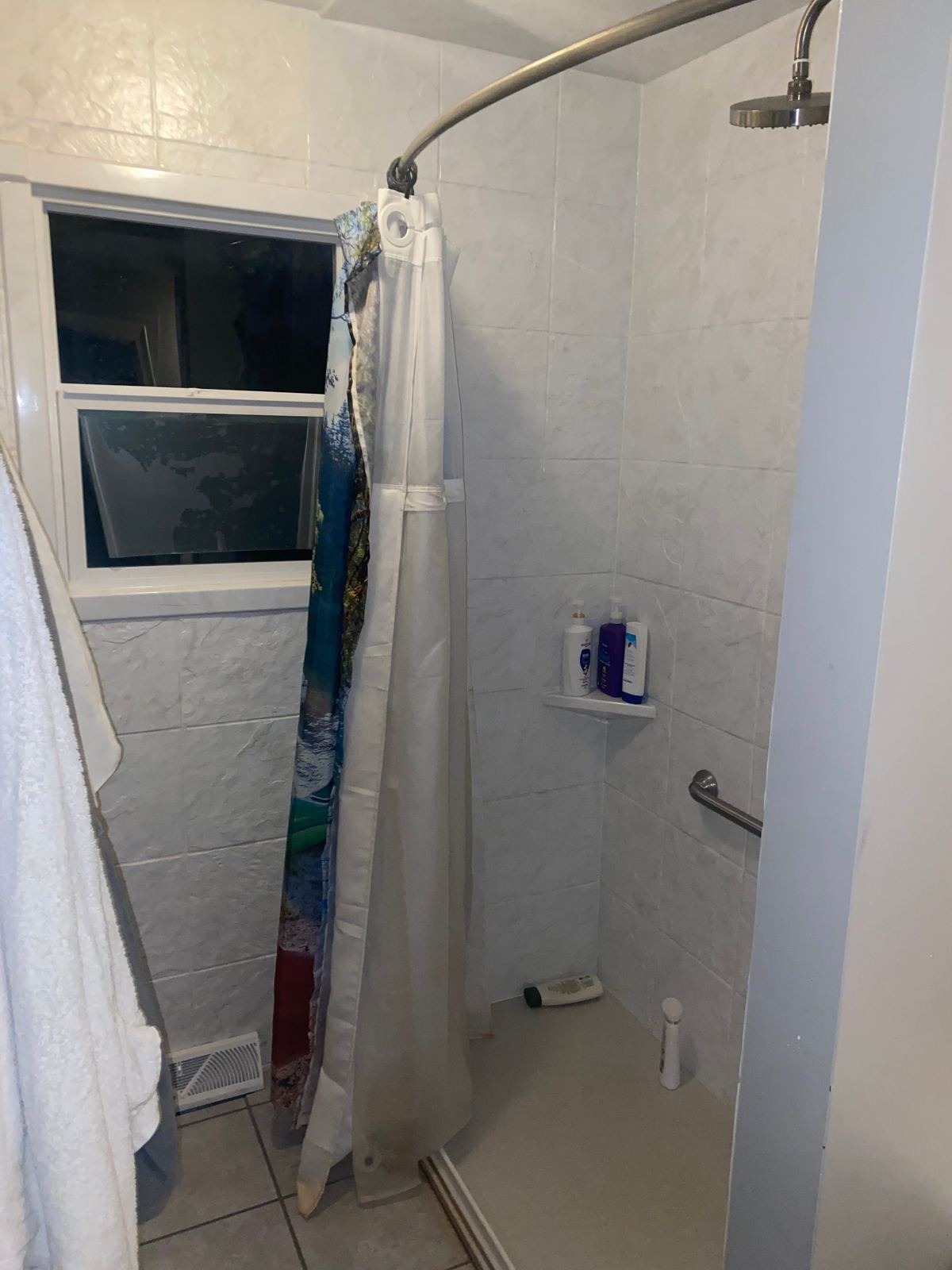 Dated white tile shower stall with curtain before renovation