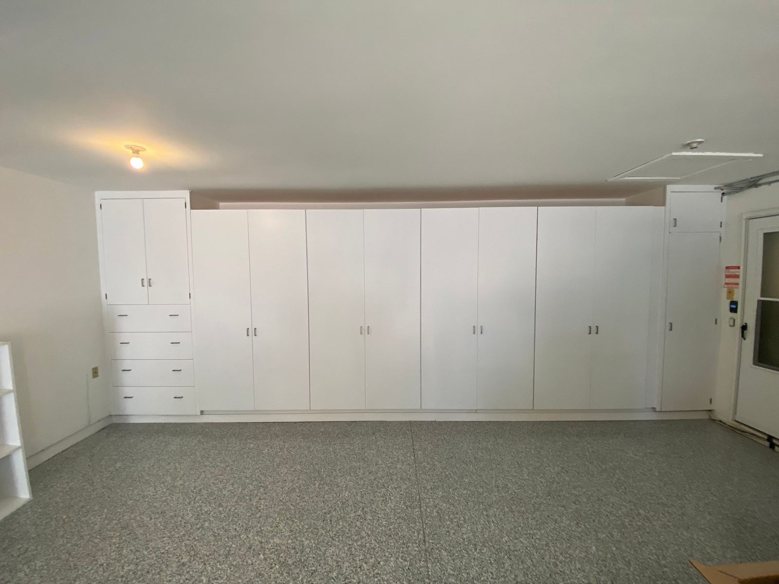 Finished garage with floor-to-ceiling white cabinetry and epoxy flake flooring