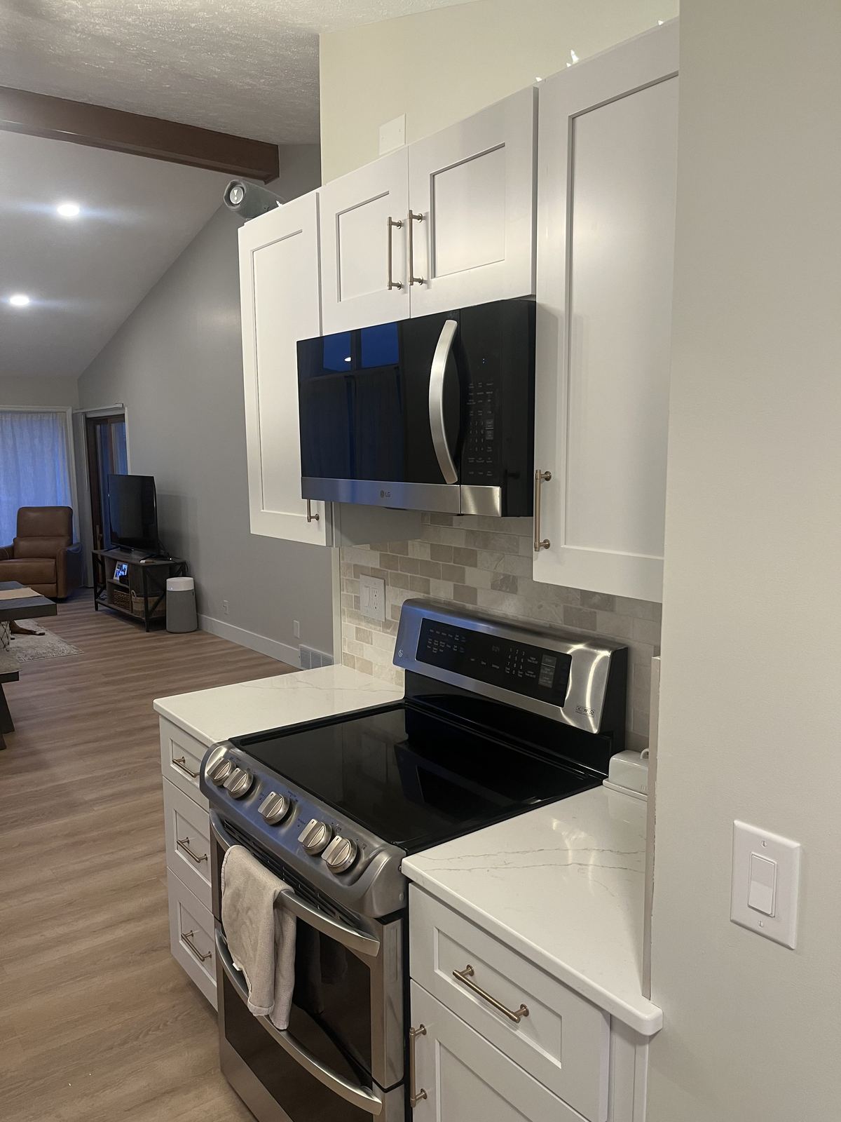 Renovated kitchen cooktop wall with white shaker cabinets, stone backsplash, quartz counters, and over-range microwave