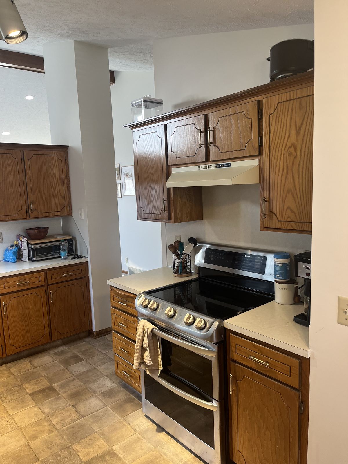 Original kitchen cooktop wall with dark oak cabinets, dated vent hood, and laminate counters before renovation
