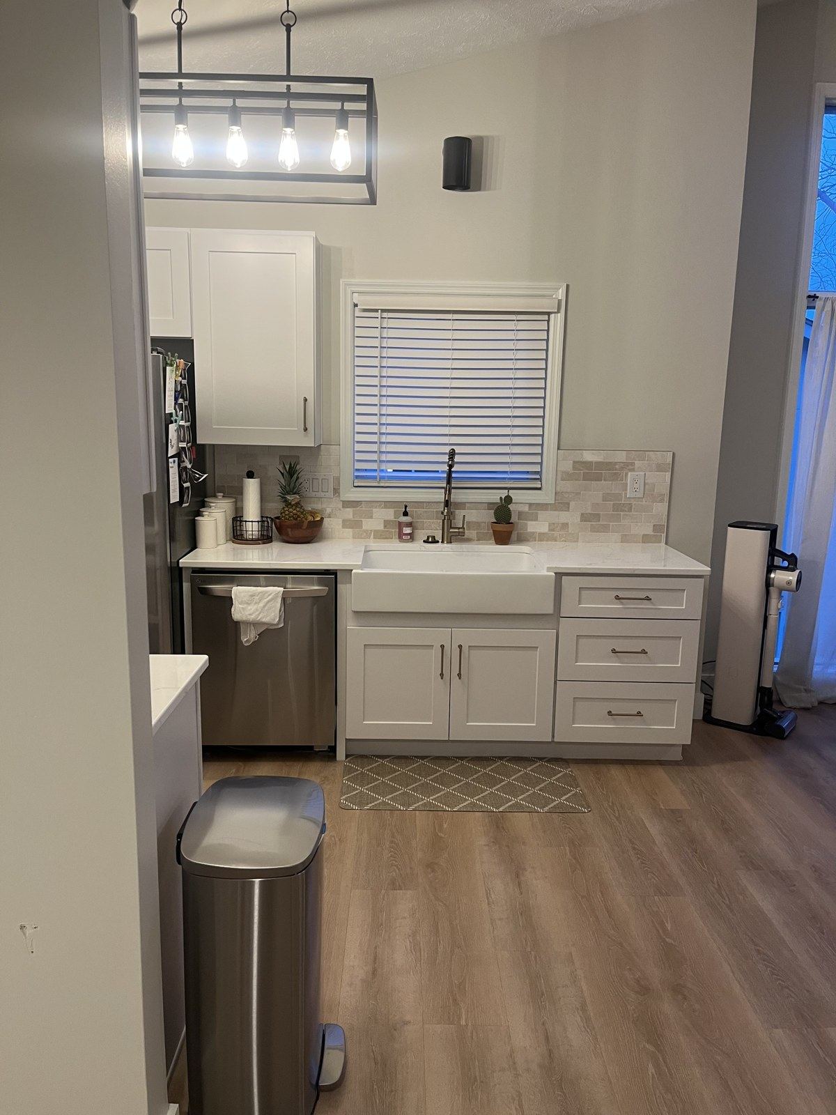 Renovated galley kitchen with white shaker cabinets, quartz counters, farmhouse sink, and wood-look flooring