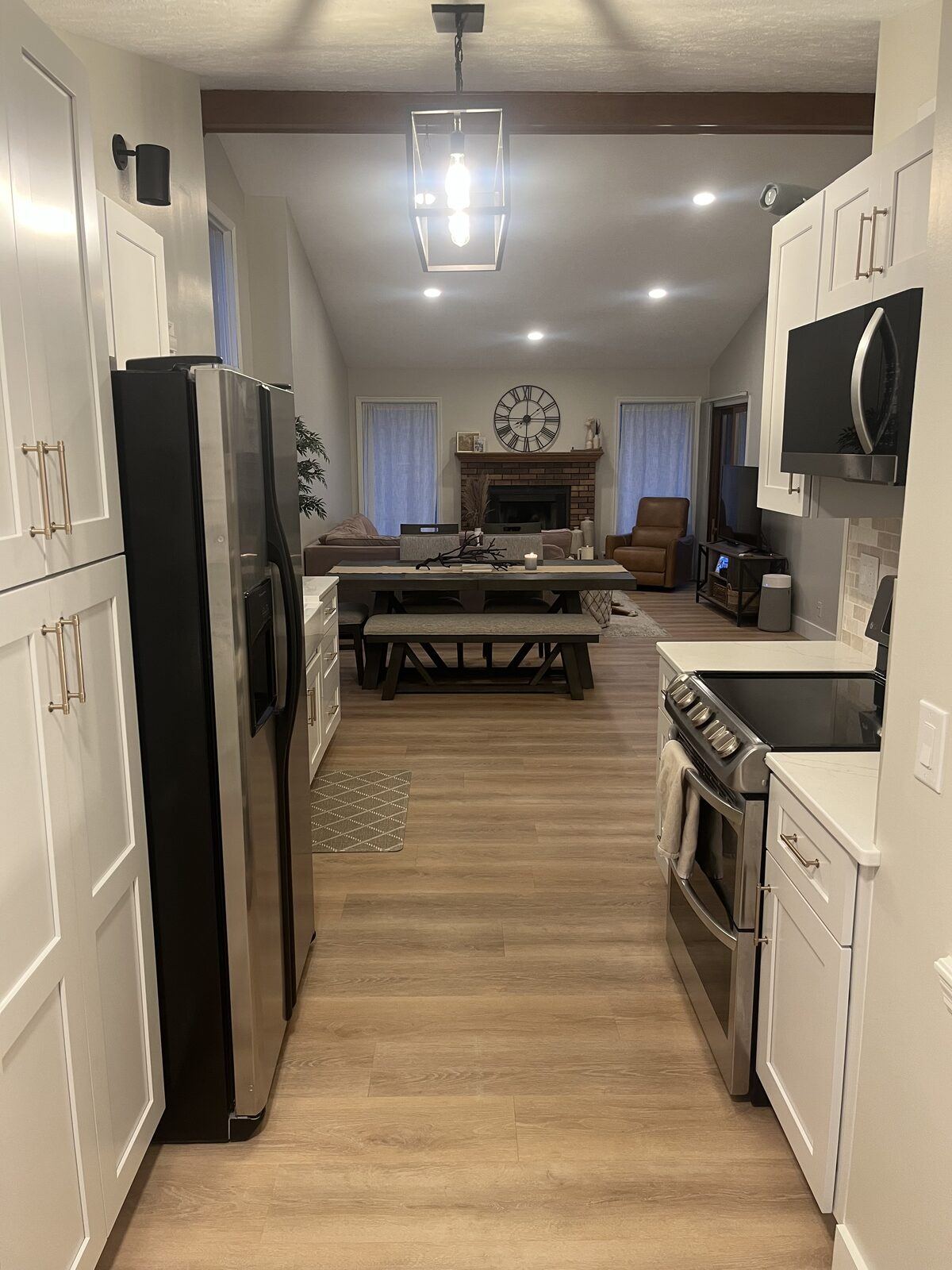Renovated galley kitchen with white shaker cabinets, quartz counters, brass hardware, lantern pendant, and wood-look flooring opening to the living room