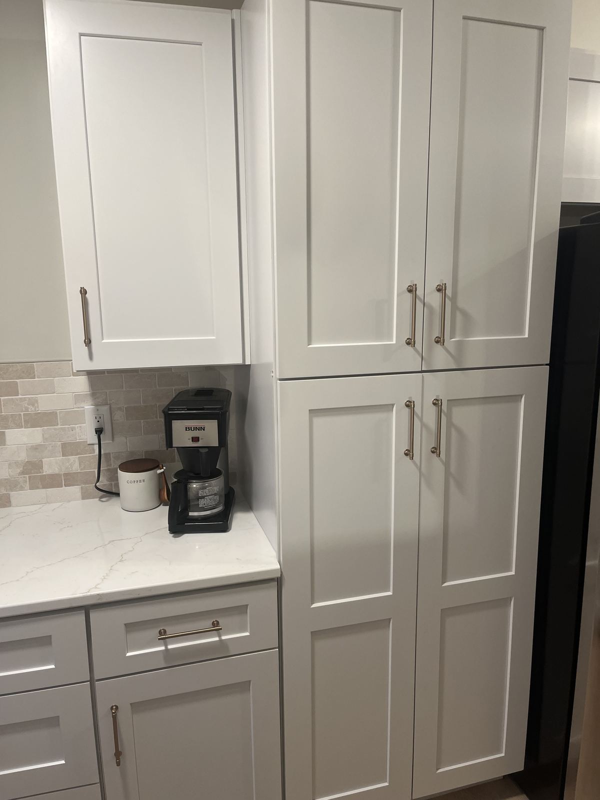 New floor-to-ceiling white shaker pantry cabinets with brass hardware, quartz coffee station, and stone tile backsplash