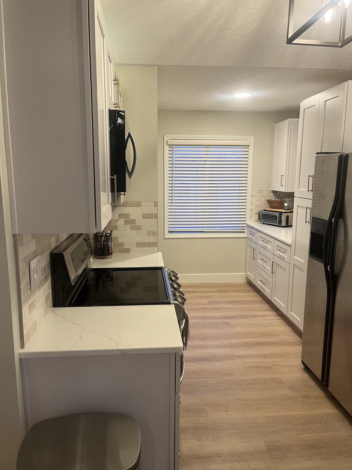 Renovated kitchen range wall with white shaker cabinets, quartz counters, tile backsplash, and wood-look flooring