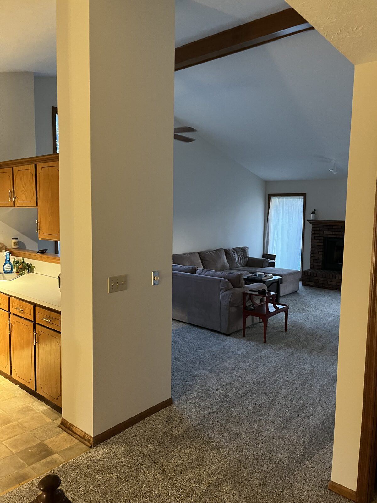 Original closed-off living room with gray carpet, oak trim, brick fireplace, and a wall dividing the kitchen before renovation