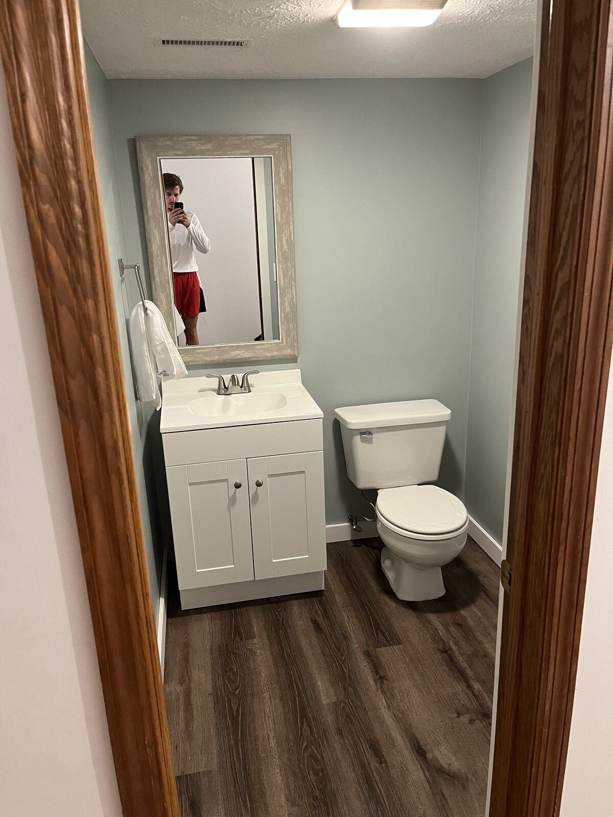 Refreshed powder bath with white shaker vanity, brushed nickel faucet, soft blue walls, framed mirror, and wood-look flooring
